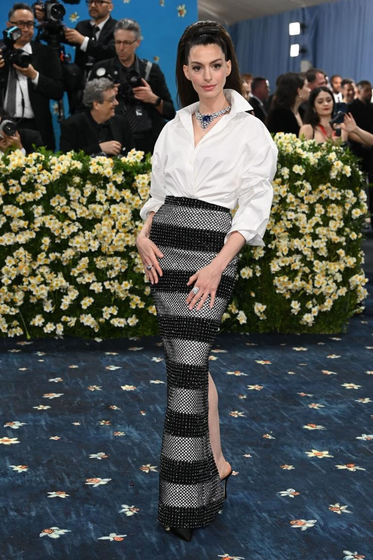 Anne Hathaway thanh lịch với sơ mi trắng và chân váy sọc ngang của Carolina Herrera. Điểm nhấn là vòng cổ kim cương cỡ đại. Ảnh: Shutterstock.