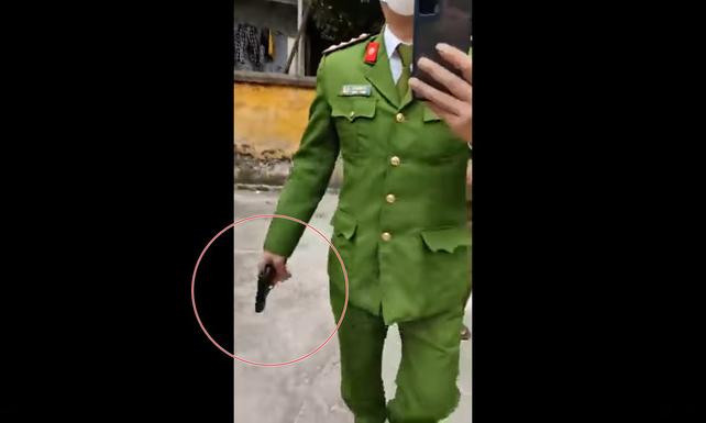 Người đàn ông mặc trang phục công an, tay cầm vật giống súng - Ảnh: Cắt từ clip. Người đàn ông mặc trang phục công an, tay cầm vật giống súng - Ảnh: Cắt từ clip.