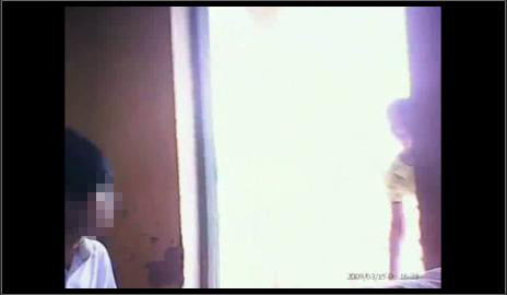 Một người phụ nữ áo vàng ném gì đó vào trong phòng thi, sau đó, một thí sinh nhặt lên. Ảnh: Chụp lại từ clip