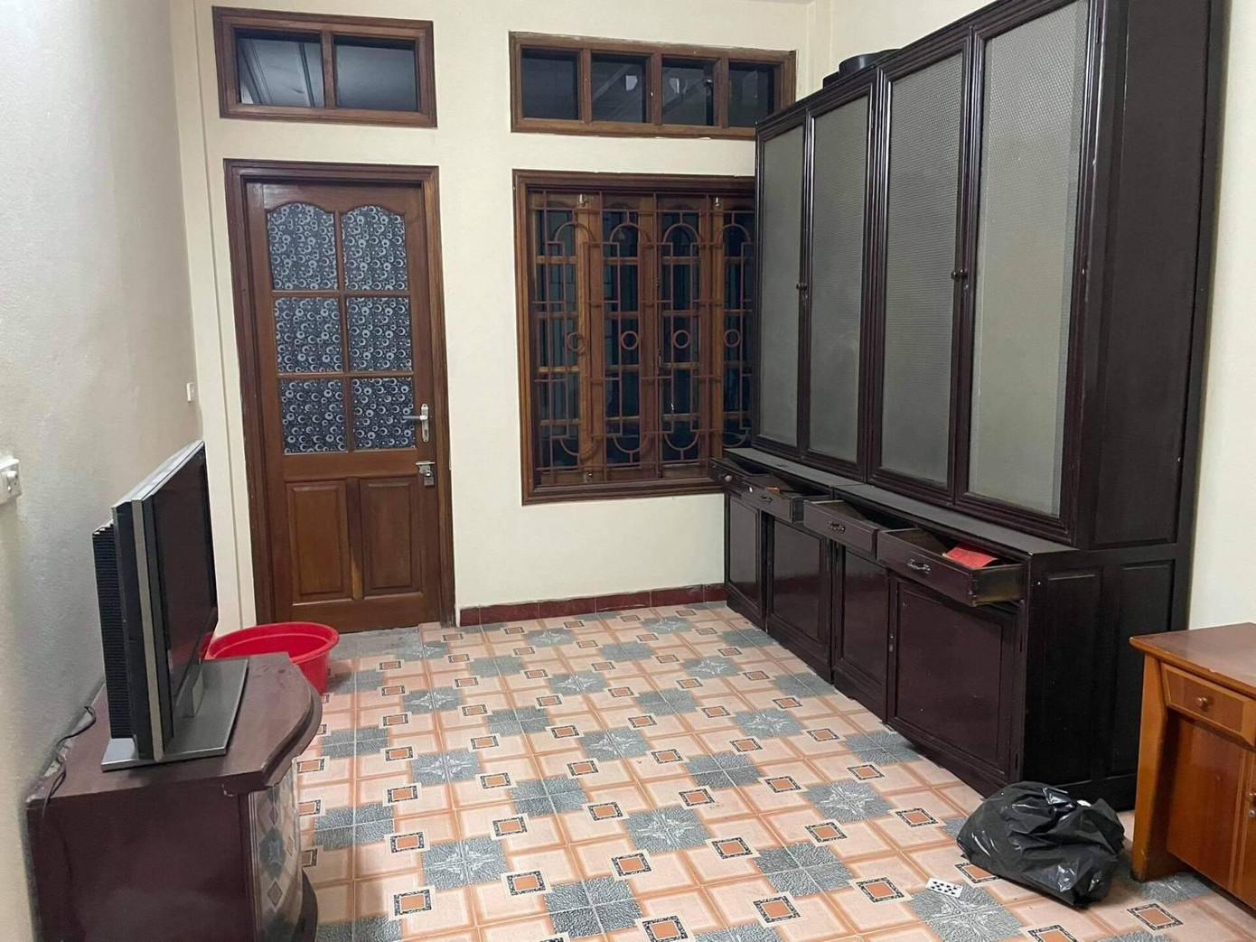 Phòng khách được sơn lại, phần cửa gỗ và cửa sổ được phá bỏ để làm thành ban công - nơi cung cấp nguồn sáng chính cho ngôi nhà. Trong phòng khách, gia chủ bỏ hết các đồ nội thất cũ như tivi, tủ gỗ, bàn gỗ, thay vào đó là kệ để sách sát tường xinh xắn, một ghế sofa trắng bên cạnh bình hoa, sàn lát gỗ để tạo điểm nhấn cho không gian.