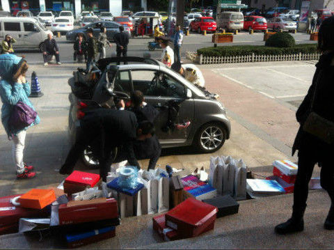 Cô gái trẻ (áo xanh) và 100 túi đựng giày, đang treo từng đôi lên chiếc ô tô của mình