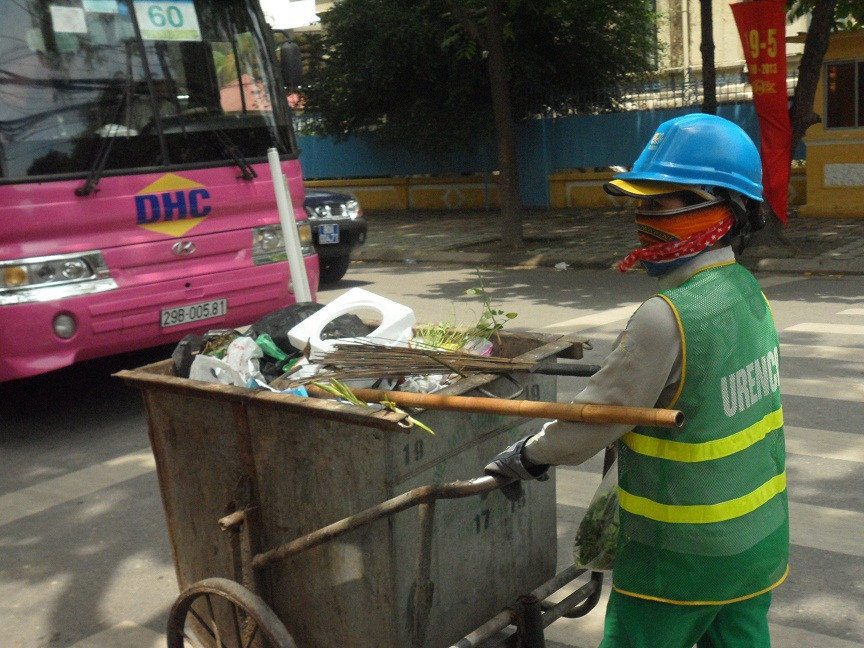 Chị lao công của Xí nghiệp môi trường đô thị Hà Nội miệt mài dọn rác trên các tuyến phố Hà Nội lúc 8h sáng. Chị vừa đẩy thùng rác to sụ vừa chia sẻ: “Những ngày trời oi bức thế này làm việc vất vả lắm, mùi nồng nặc hơn nên càng độc hại hơn”