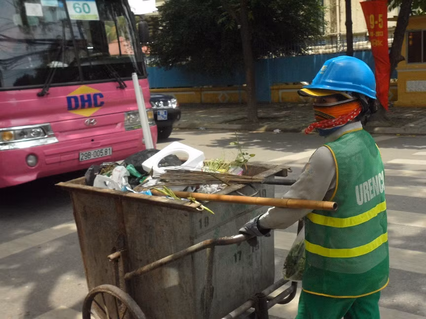 Chị lao công của Xí nghiệp môi trường đô thị Hà Nội miệt mài dọn rác trên các tuyến phố Hà Nội lúc 8h sáng. Chị vừa đẩy thùng rác to sụ vừa chia sẻ: “Những ngày trời oi bức thế này làm việc vất vả lắm, mùi nồng nặc hơn nên càng độc hại hơn”