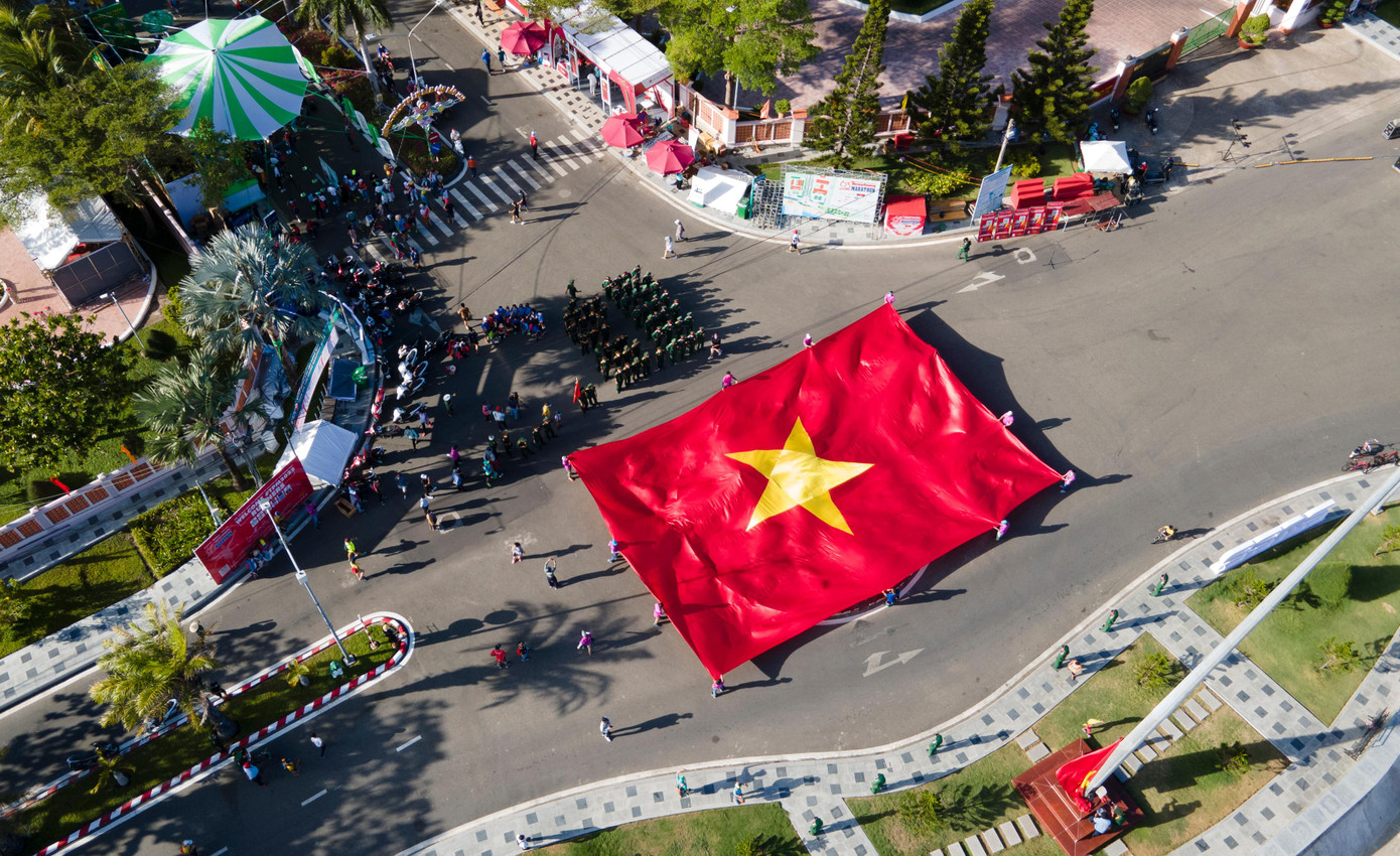 Các vận động viên, tình nguyện viên trải lá cờ Tổ quốc rộng 300m2 trên Quảng trường Cột cờ. Ảnh: Như Ý