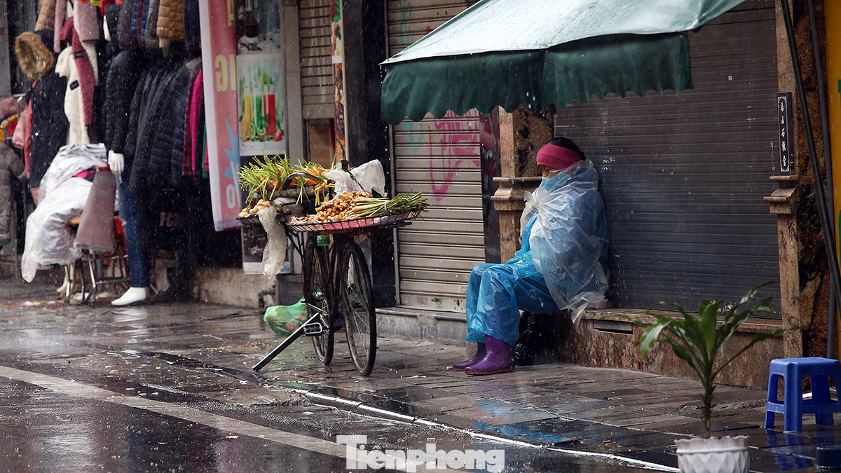 Cô Lan bán hàng rau củ ngồi co ro trên vỉa hè phố Hàng Đào tránh mưa rét.