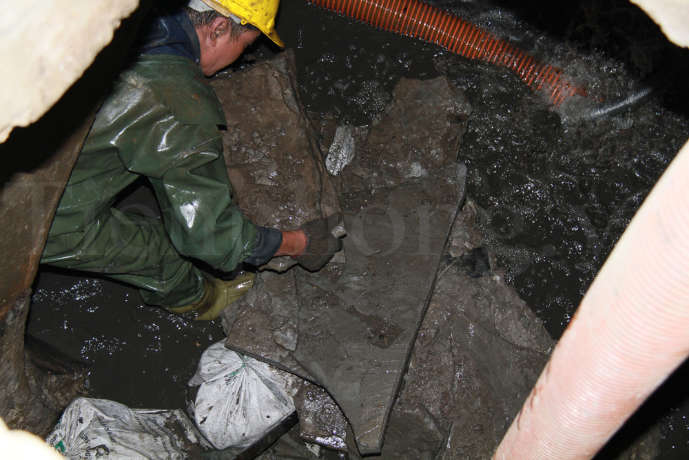 Anh Nguyễn Anh Tuấn khệ nệ bê những tảng xi măng đông đặc từ trong thành cống ra ngoài. Ảnh: Trường Phong