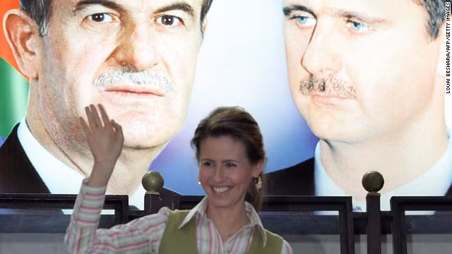 Đệ nhất phu nhân Syria đứng dưới tấm ảnh lớn của tổng thống Assad và cố tổng thống Hafez al-Assad tháng 5/2006