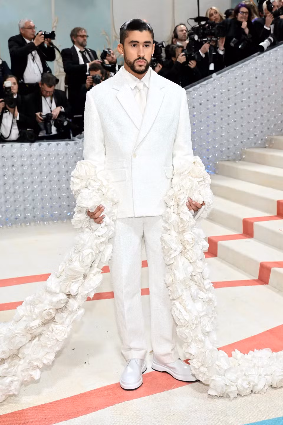 Bad Bunny diện nguyên set đồ trắng kem với chất liệu vải tweet, đi kèm với khăn choàng dài kết hoa hồng. Một nét chấm phá lạ lẫm cho thảm đỏ Met Gala 2023.