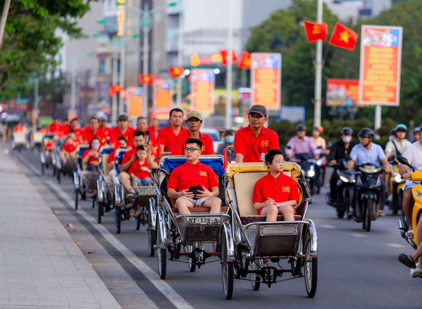 Trên những chiếc xích lô chở đầy nụ cười và tinh thần Việt, các tài xế và du khách cùng rực rỡ trong sắc đỏ, tạo nên một hành trình phố phường đầy cảm xúc và tự hào.