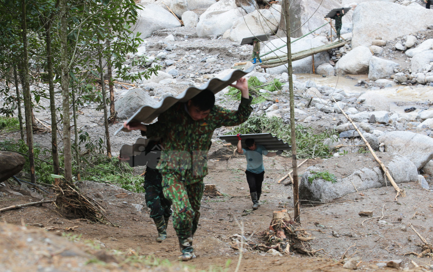 Lực lượng quân đội cùng người dân vác những tấm lợp đi qua cầu tre bắc tạm.