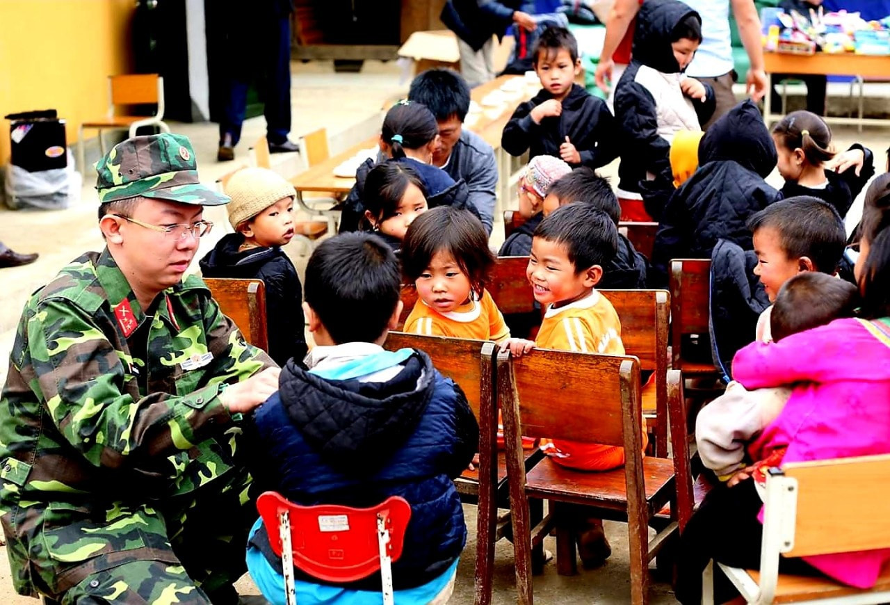Nhà báo Hoàng Trường Giang ân cần đeo khăn cho em nhỏ trong một buổi thiện nguyện tại điểm trường vùng cao, ánh mắt trẻ thơ trong sáng và rạng rỡ niềm vui.