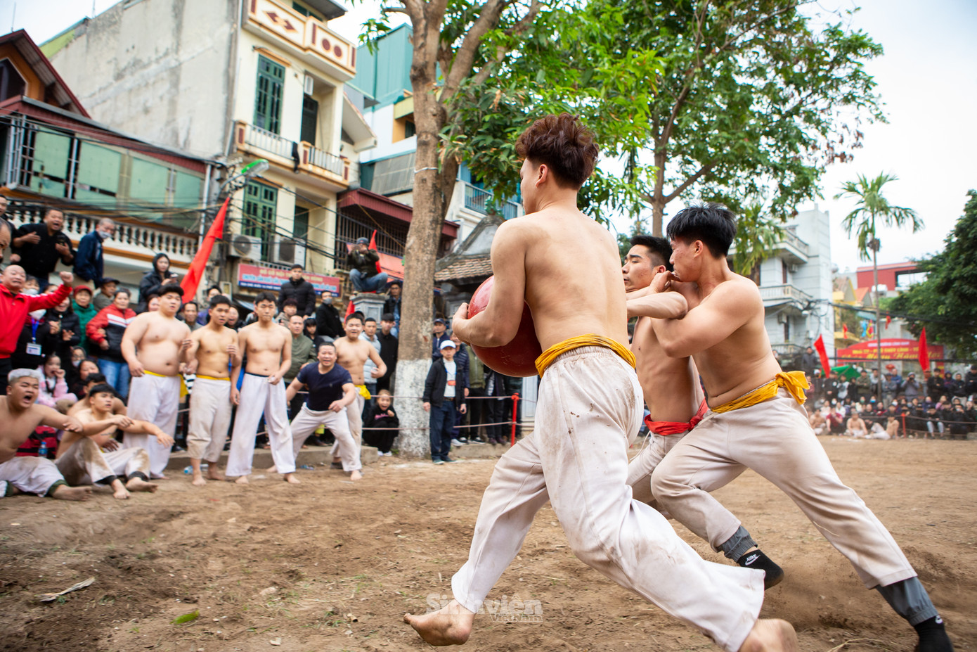 Đoạt cầu từ tay đội đỏ, một vận động viên đội vàng bứt tốc về phía hố để ghi điểm trong khi đồng đội cản trở đối thủ cướp cầu.