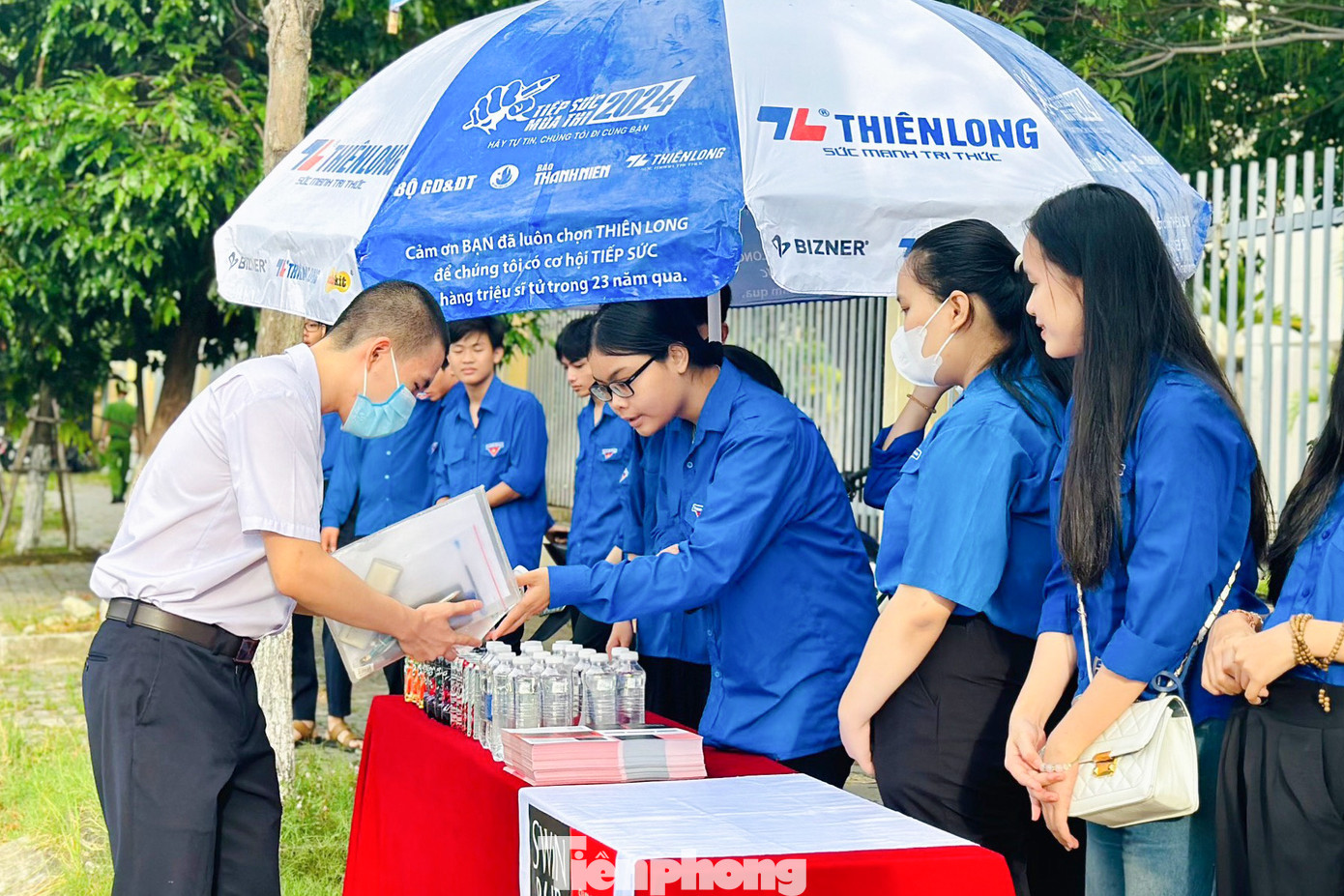 Từ sáng sớm, tại các điểm thi, những bóng "áo xanh" đã túc trực để chuẩn bị nước đóng chai (lột bỏ tem nhãn), dụng cụ học tập như bút chì, tẩy, bút bi..., quạt tay, bánh mì để phát cho thí sinh và người nhà.