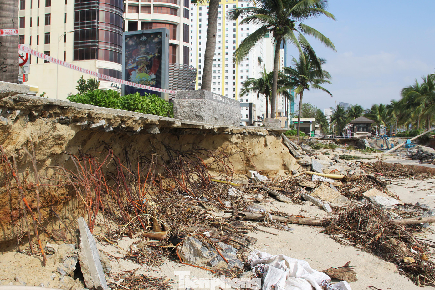 Sóng đánh toác bờ kè, lộ ra cả nền đất đá, rễ cây xơ xác dưới lòng đất. Cành cây khô, cát, gạch lát, các loại rác... nằm ngổn ngang dưới hố sụt lún.