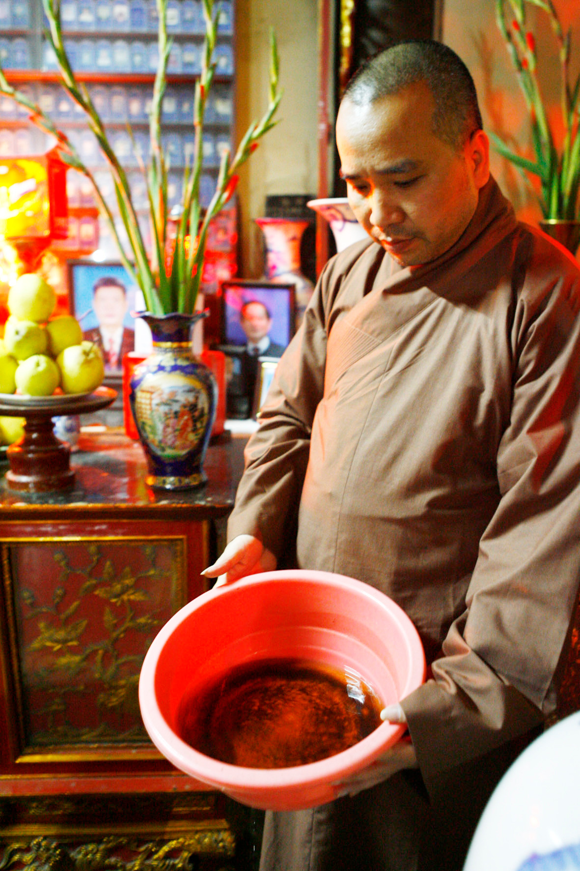 Đại đức Thích Tâm Kiên với chậu hứng nước mưa dột. Ảnh: Hồng Vĩnh