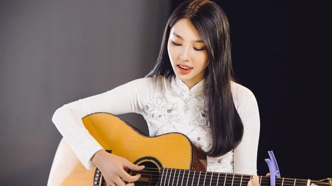 Thùy Tiên diện áo dài trắng, vừa đàn vừa hát ca khúc Hello Việt Nam.