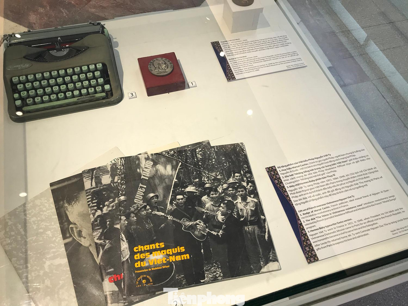 Bộ tặng phẩm của Việt kiều Pháp Nguyễn Viết Tỵ, gồm Huy hiệu Marcel Cachin; đĩa hát Những tiếng hát trong các bưng biền Việt Nam; máy chữ Hermes Baby phiên bản Thuỵ Sỹ tặng Chủ tịch Hồ Chí Minh. Nguyễn Việt Tỵ sang Pháp năm 1921. Năm 1946, khi Chủ tịch Hồ Chí Minh và phái đoàn ngoại giao Việt Nam đến Paris trong chuyến thăm chính thức Cộng hoà Pháp, anh vinh dự trở thành đầu bếp nấu ăn phục vụ Người và phái đoàn. Sau khi Bác Hồ về nước, anh đã gửi đồng chí Nguyễn Đức Thọ mang từ Paris về tặng Người số tặng phẩm nói trên để bày tỏ tình cảm và sự ngưỡng mộ. Ảnh: Trường Phong