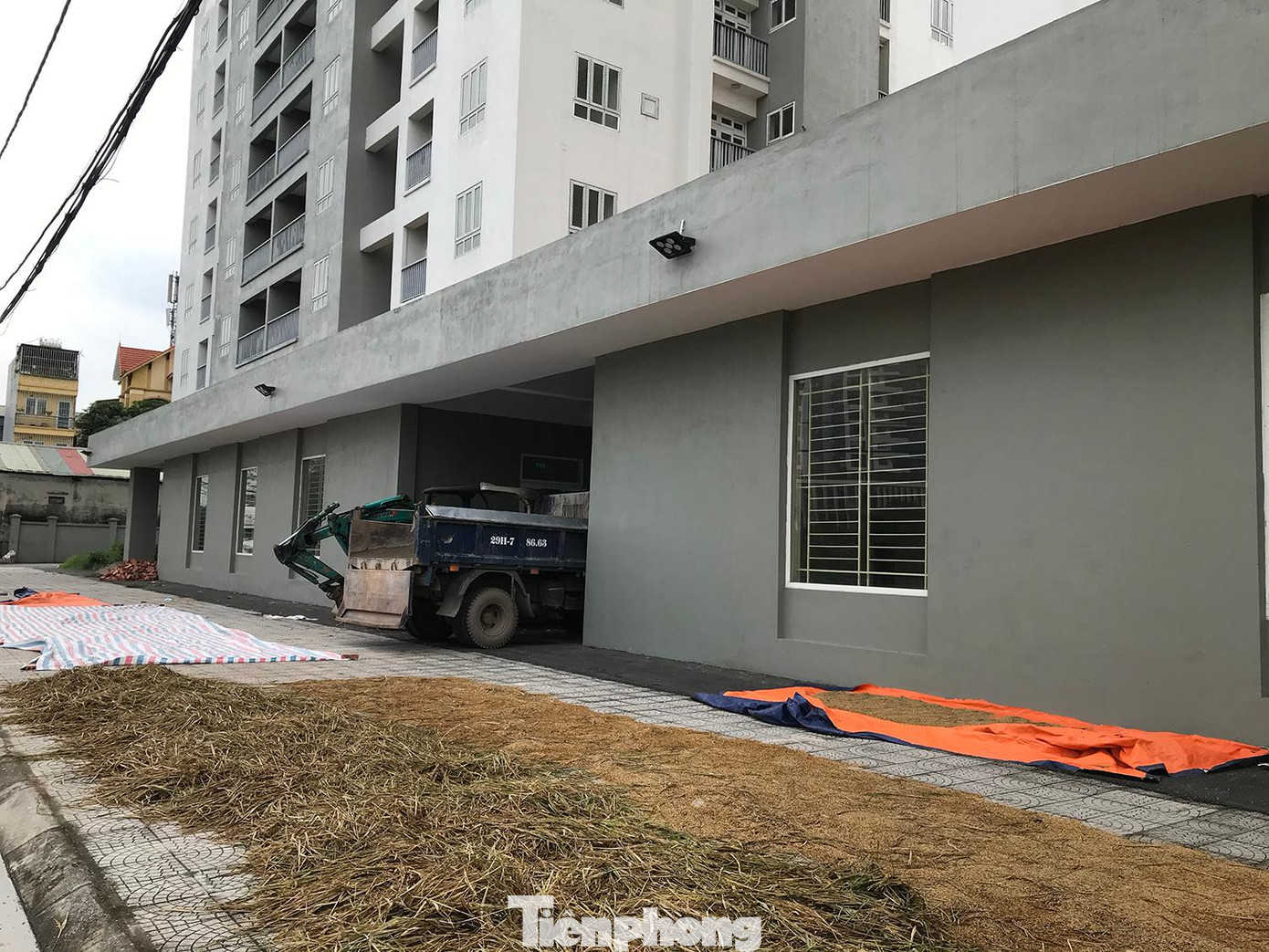 Vỉa hè trước cửa toà chung cư được tận dụng làm nơi phơi thóc. Khu vực cửa chính ra vào toà nhà án ngữ nhiều máy móc. Ảnh: Trường Phong