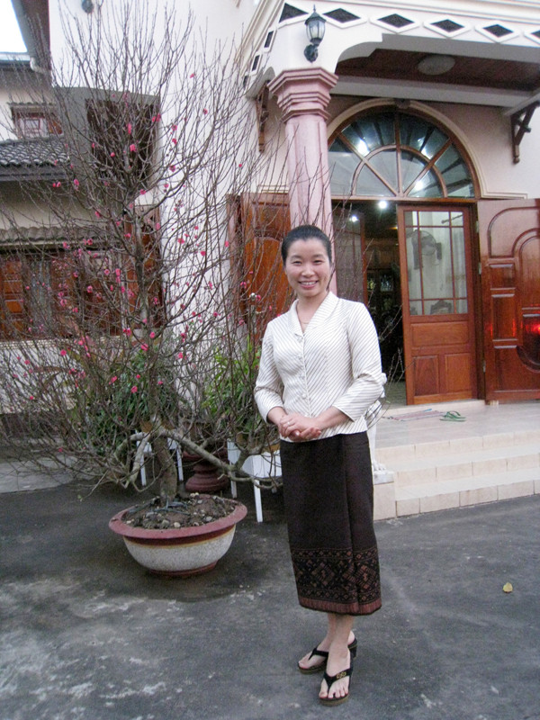 Chị Ngọc Ánh bên cạnh cây đào Nhật Tân trước hiên nhà ở tỉnh lỵ Bolikhamxay