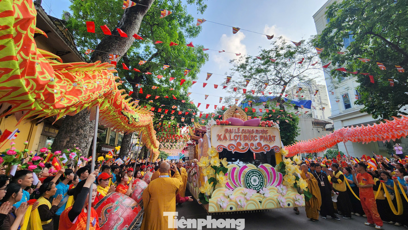 Phật tử trong trang phục chỉnh tề, tay cầm cờ và hoa sen, thành kính xếp hàng trước cổng chùa.