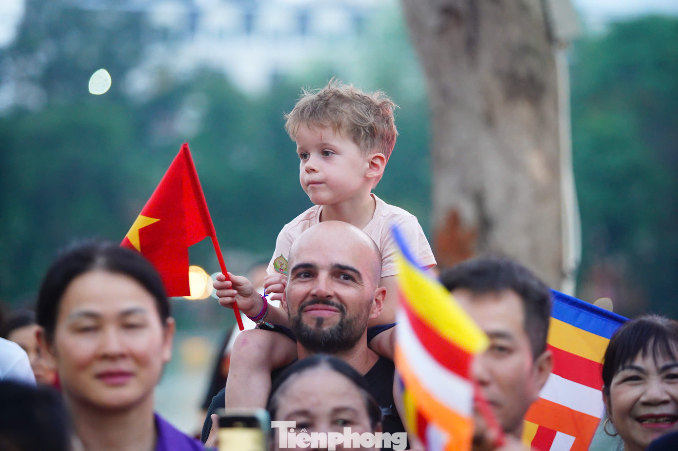 Hàng nghìn người cầm cờ Tổ quốc, cờ Phật giáo đứng chờ đoàn xe. Du khách quốc tế cũng hòa vào dòng người.