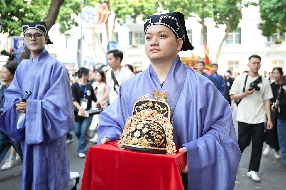 Một tình nguyện viên bê mũ Cửu Long - mô phỏng từ thành quả dự án phục dựng của Bảo tàng Lịch sử Việt Nam năm 2010 và cuốn sách Ngàn năm áo mũ năm 2013.