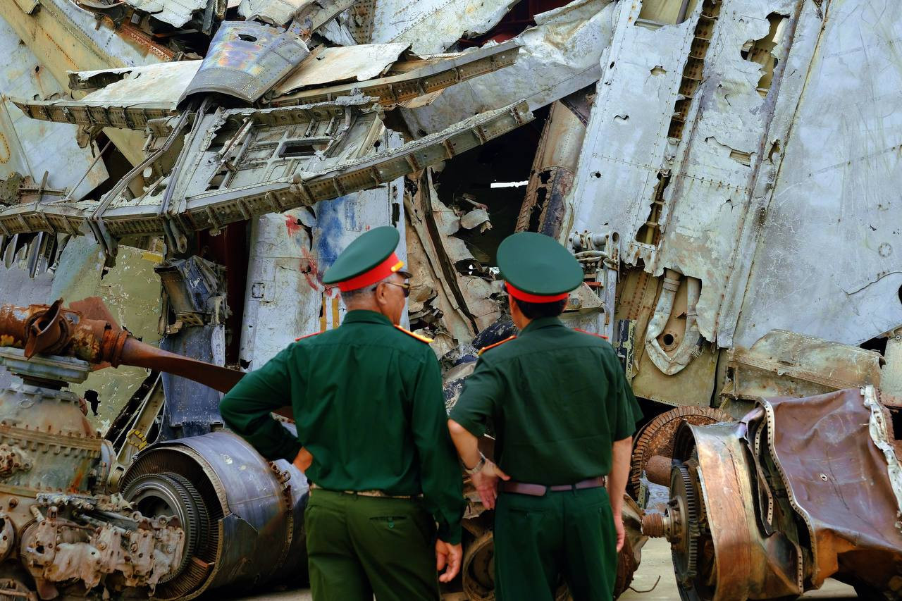 Hai cựu chiến binh đứng trước mảnh xác máy bay của Pháp, Mỹ và động cơ máy bay Hellcat. Hellcat là máy bay do Mỹ chế tạo, viện trợ cho Pháp sử dụng trong chiến tranh xâm lược Việt Nam. Máy bay này đã bị bắn rơi tại mặt trận Điện Biên Phủ năm 1954.