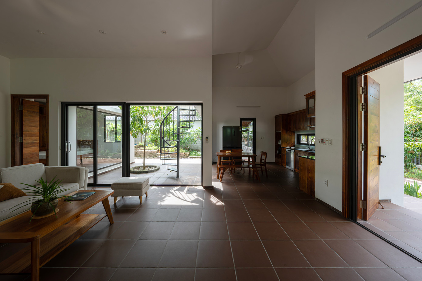 Hành lang được thiết kế với các cấp độ so le theo địa hình dốc thoai thoải của khu đất, kết nối với một sân nhỏ, dẫn đến phòng khách, bếp và phòng ngủ. Thiết kế này làm phong phú thêm trải nghiệm sống hàng ngày, tạo ra những khoảnh khắc thú vị nhất trong những ngày mưa hay nắng.