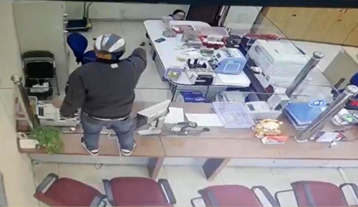 Kẻ cướp chĩa súng vào nhân viên ngân hàng yêu cầu bỏ tiền vào ba lô. Ảnh cắt từ clip Kẻ cướp chĩa súng vào nhân viên ngân hàng yêu cầu bỏ tiền vào ba lô. Ảnh cắt từ clip