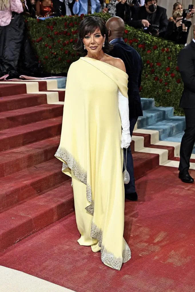 Mẹ của chị em Kardashian-Jenner, bà Kris Jenner, diện váy vàng lệch vai dáng suông của thương hiệu Oscar de la Renta, đi găng tay trắng bóng mượt và để mái tóc kiểu cũ, trông sang trọng và thanh lịch hợp tuổi tác.