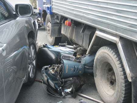 Xe máy bị cuốn vào gầm ô tô.