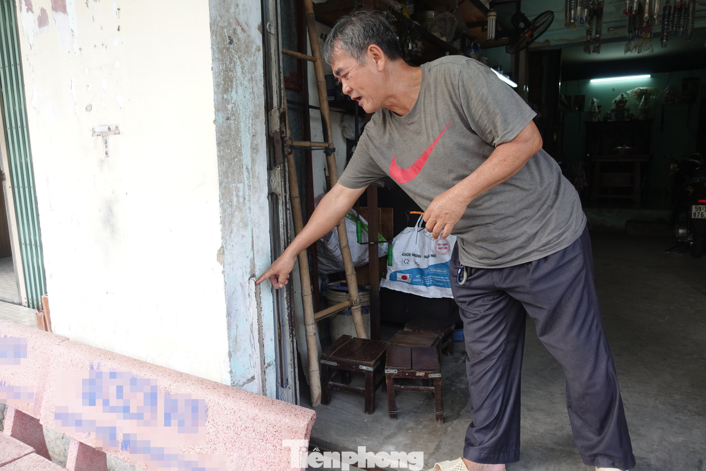 &quot;Đến nay mực nước ngày càng cao, nền thì không thể tiếp tục nâng lên được nữa vì trần nhà đang thấp lắm rồi ! Do đó tôi phải tự thiết kế một tấm bảng thép có sẵn khe rãnh để lắp đặt trước cửa nhằm ngăn nước và rác thải tràn vào nhà khi có mưa lớn&quot;- ông Long chia sẻ. (Ảnh: ông Long chỉ cho Phóng viên xem nơi đặt công cụ ngăn nước, chống ngập cho căn nhà)