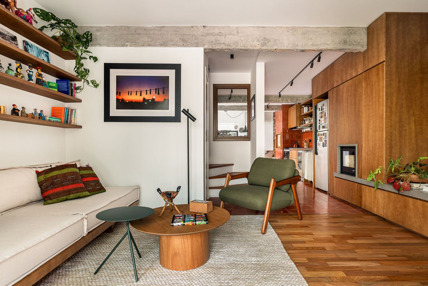 Dọc theo một bên tường trong phòng khách là hệ tủ liên hoàn, chi tiết về cả công năng lẫn thẩm mỹ. Đây vừa là kệ tivi, ghế ngồi tích hợp, vừa kéo dài thành bàn bếp, tủ chứa đồ liền mạch từ phòng khách sang bếp. Đặc biệt, một lò sưởi nhỏ được đặt tích hợp khéo léo trở thành điểm nhấn ấm cũng giữa không gian hiện đại.