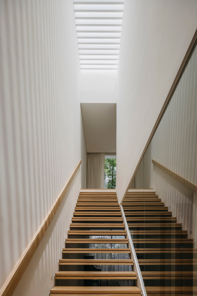 Một cầu thang đặc trưng chạy dọc theo tường chung của ngôi nhà, được chiếu sáng liên tục bởi giếng trời phía trên, đảm bảo không gian bên trong không luôn ngập tràn ánh sáng.