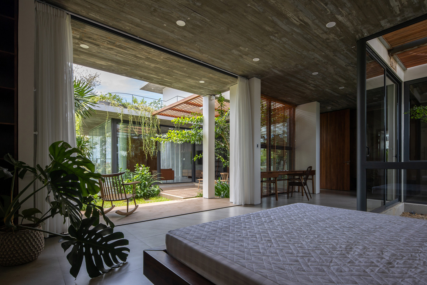 Tấm kính trượt lớn và rèm vải ngăn cách không gian bên trong và bên ngoài phòng ngủ. Với thiết kế này, gia chủ có thể dễ dàng mở cửa ra để tận hưởng không khí tự nhiên khi cần hoặc đóng lại nếu muốn có không gian riêng tư.