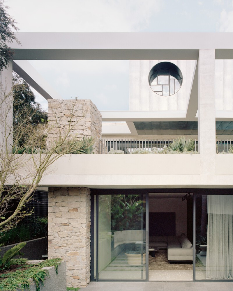 Ngay từ mặt tiền, người nhìn sẽ bị ấn tượng bởi mảng bê tông như lơ lửng trên khu vườn phía trước, kết hợp dải kính hoa văn mảnh mai.