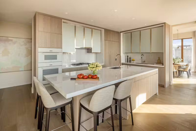 Bếp ăn cao cấp được thiết kế như một không gian nghệ thuật với cửa sổ kính lớn hướng Bắc, đảo bếp cỡ lớn cùng hệ tủ gỗ tần bì nhuộm màu riêng biệt, nổi bật với tủ kính gợn sóng phía trên và mặt bếp cùng tường ốp bằng đá cẩm thạch Bianco Ice sáng bóng.