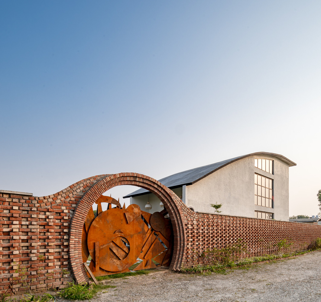 Cánh cổng thép Corten đỏ vừa là lối vào vừa là tác phẩm nghệ thuật nằm nổi bật giữa bức tưởng gạch mộc.