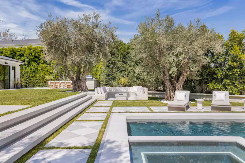 Ngay từ sảnh dẫn vào nhà là những cây ô liu lớn đặc trưng của địa phương. Bên cạnh là một hồ bơi có thác nước, bếp ngoài trời, giàn pergola và các khu lounge được bố trí khéo léo tạo nên phong cách một khu nghỉ dưỡng tại nhà đích thực.