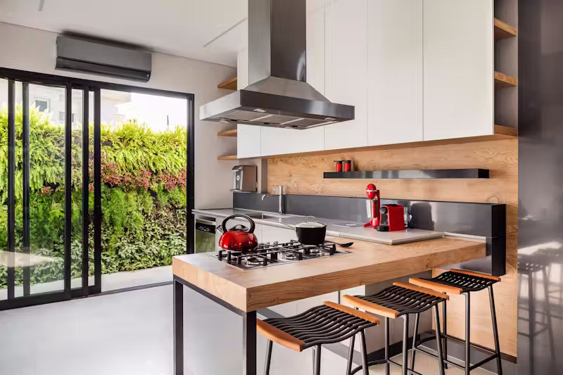 Ở tầng trệt, các khu vực chức năng đều hiện ra trong tầm mắt, đặc biệt là khu bếp được thiết kế như "trái tim" của ngôi nhà. Tại đây, một khung cửa mở phía sau giúp không gian này đóng vai trò cầu nối linh hoạt giữa nội thất và khu vực ngoài trời. Một điểm thú vị khác là việc sử dụng các cánh cửa ẩn được tích hợp cùng tấm ốp gỗ tạo nên vẻ tối giản, tinh gọn.