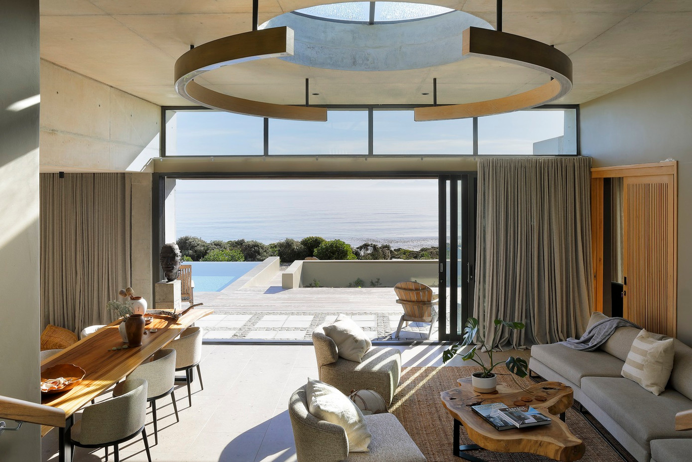 Ngay từ lối vào, tiền sảnh cao hai tầng với những ô cửa kính kịch trần tạo cảm giác rộng mở, dẫn ánh nhìn trực tiếp ra đường chân trời của đại dương bao la. Điểm nhấn tại đây chính là giếng trời hình tròn kết hợp với đèn thả trang trí, không chỉ kết nối các khu vực sinh hoạt mở mà còn nhấn mạnh sự giao thoa giữa ánh sáng và chất liệu, nâng cao giá trị thẩm mỹ và cảm giác ấm cúng cho không gian.