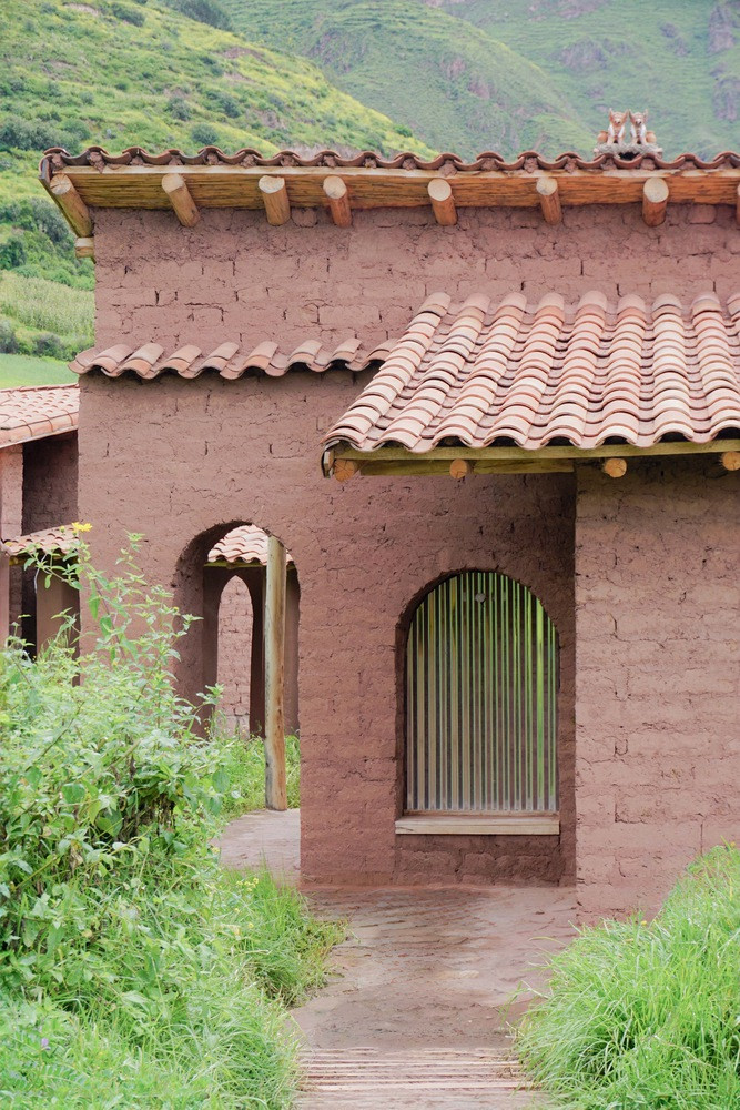 Mặt tiền của công trình nằm ở phía Đông, trải dài theo dốc đất và được chia thành hai phần phụ: tầng trên là lối vào, kho chứa và nhà vệ sinh khô; tầng chính là khi bếp, phòng ăn và sinh hoạt chung, kết hợp sân trong riêng biệt.