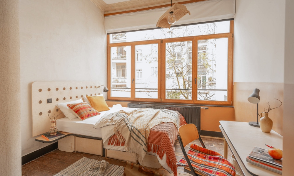 Phòng ngủ 16m2 được thiết kế với tông màu be có cửa sổ lớn đón sáng kết hợp với nội thất đỏ, cam. (Ảnh: Cohabs)