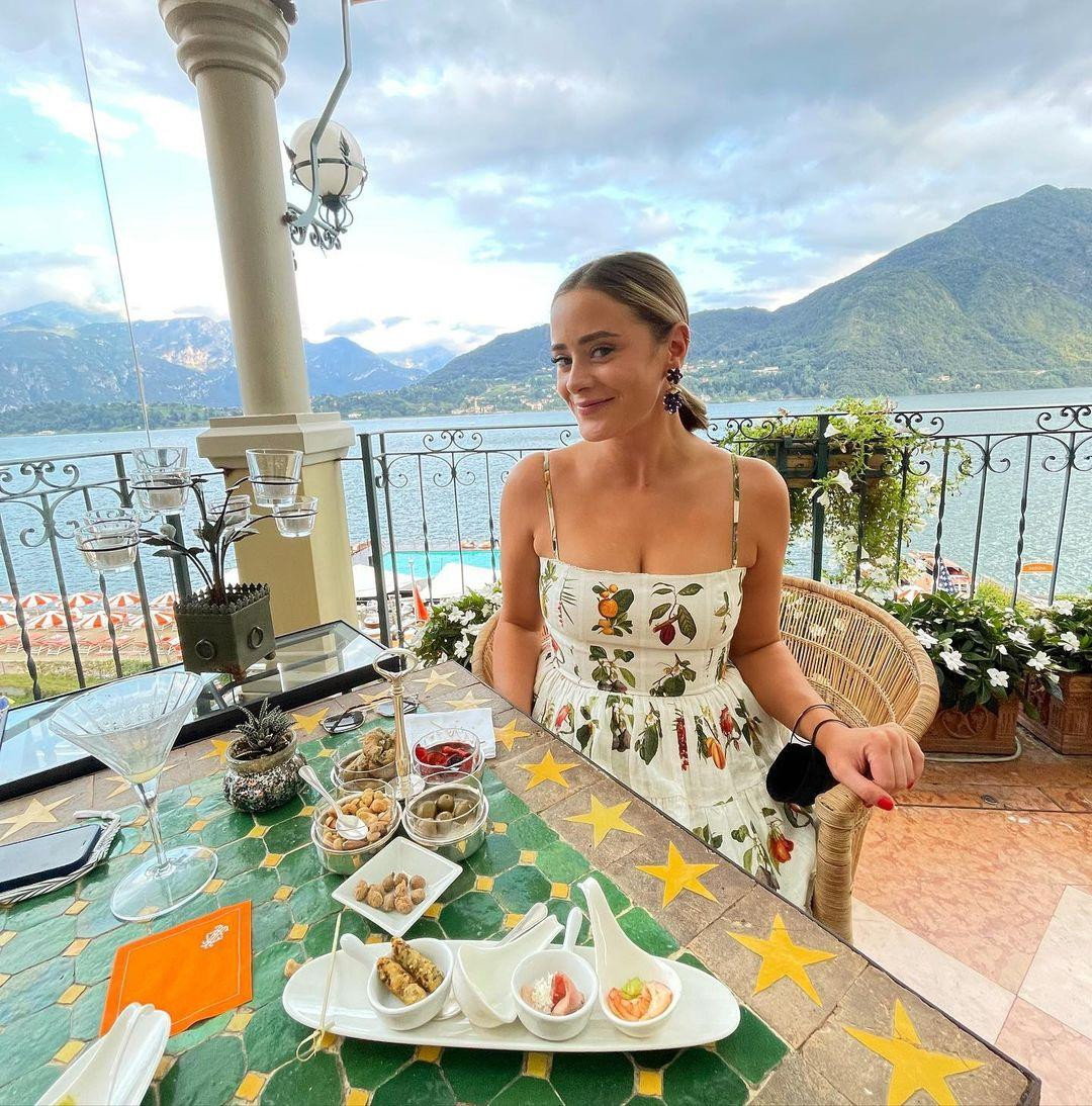 Trên Instagram, người đẹp chia sẻ bức ảnh thưởng thức đồ ăn nhẹ trên ban công khách sạn. Cô mặc váy hai dây trắng họa tiết trái cây, khéo léo che khuyết điểm ở vòng hai và tôn vòng một đầy đặn.