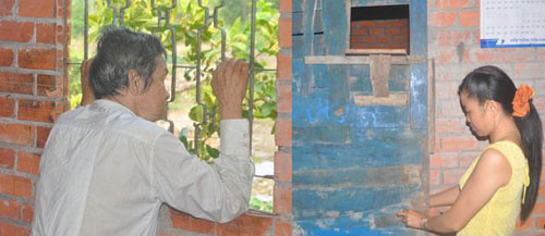 Ông Chính nhìn ra khung cửa sổ từ “phòng giam“. Con dâu ông Chính mở cánh cửa nơi nhốt cha chồng - Ảnh: THÀNH BẮC (Tuổi Trẻ)