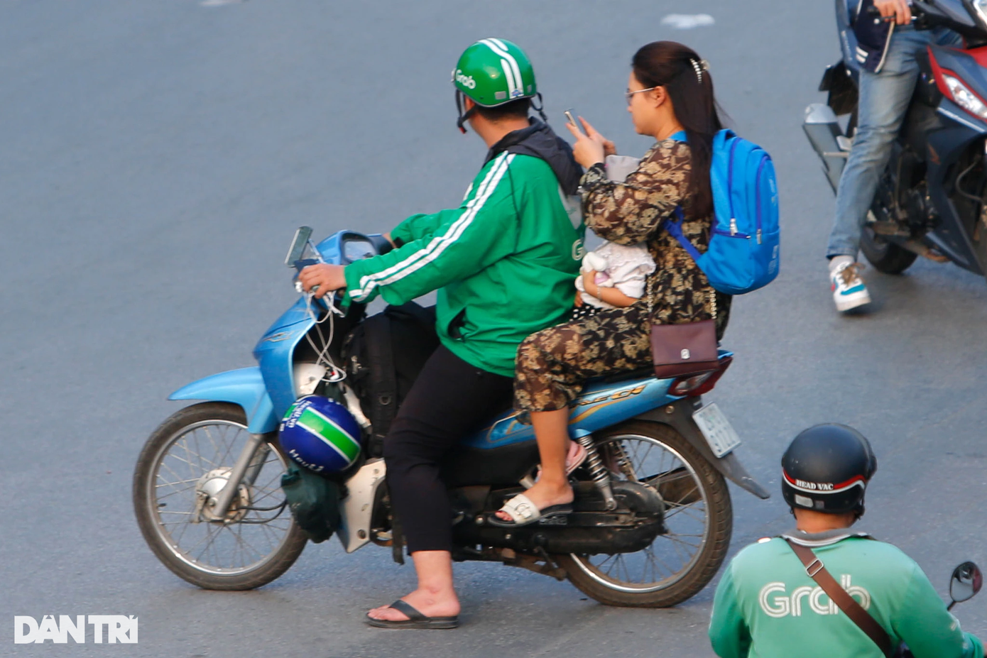 Một trường hợp lái xe mặc trang phục Grab chở phụ nữ và trẻ nhỏ di chuyển trên đường phố đông đúc, nhưng không đội mũ bảo hiểm cho khách.
