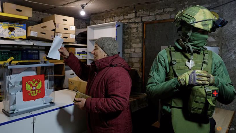 Một người dân đi bỏ phiếu vào thùng ngay cạnh lính gác ở thành phố Avdiivka, vùng Donetsk, ngày 16/3. (Ảnh: Reuters)