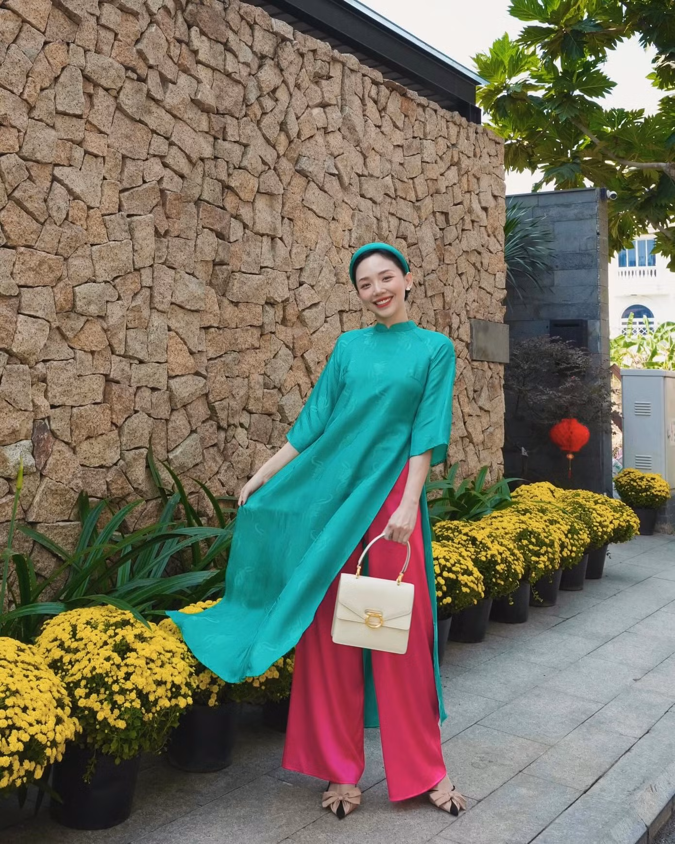 Tóc Tiên trẻ trung với tà áo dài dáng suông màu xanh, kết hợp với quần màu hồng nổi bật.