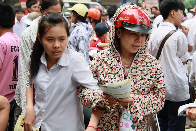 Phải rất khó khăn, bậc phụ huynh này mới kéo được con gái mình ra khỏi vòng vây của những người phát tờ rơi. Trên tay hai mẹ con đều có một tập tờ rơi. Ảnh: Trường Phong