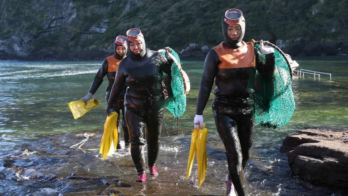 Một nhóm Haenyeo (nữ thợ lặn) đi bộ trên bãi biển sau khi lặn ở đảo Jeju, Hàn Quốc. (Ảnh: Tân Hoa Xã)